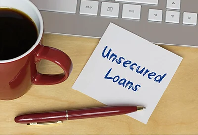 Sticky note reading Unsecured Loans beside a coffee mug